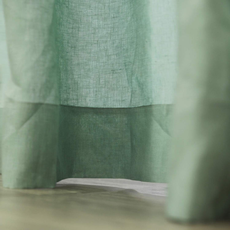 Close-up texture of handcrafted sage green linen curtain fabric showing natural weave