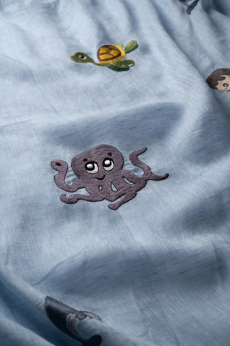 Close-up view of hand-embroidered turtle and mermaid details on natural linen fabric showing intricate stitching and aquatic motifs