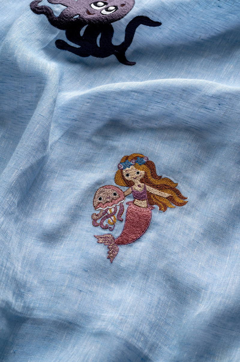 Natural sunlight filtering through aquatic embroidered linen curtains creating soft, diffused lighting in child's nursery room
