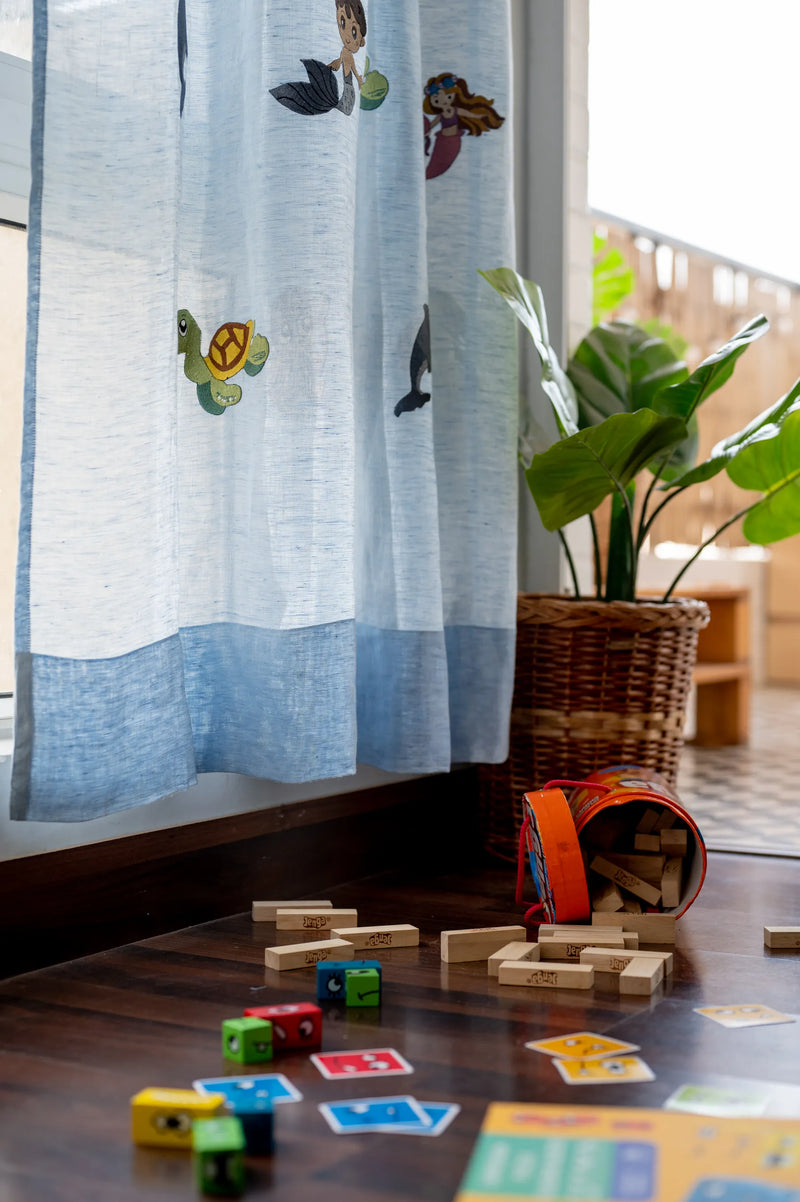 Aquatic embroidered linen sheer curtains with hand-stitched turtles, mermaids and dolphins in serene blue hanging in bright nursery with natural lighting